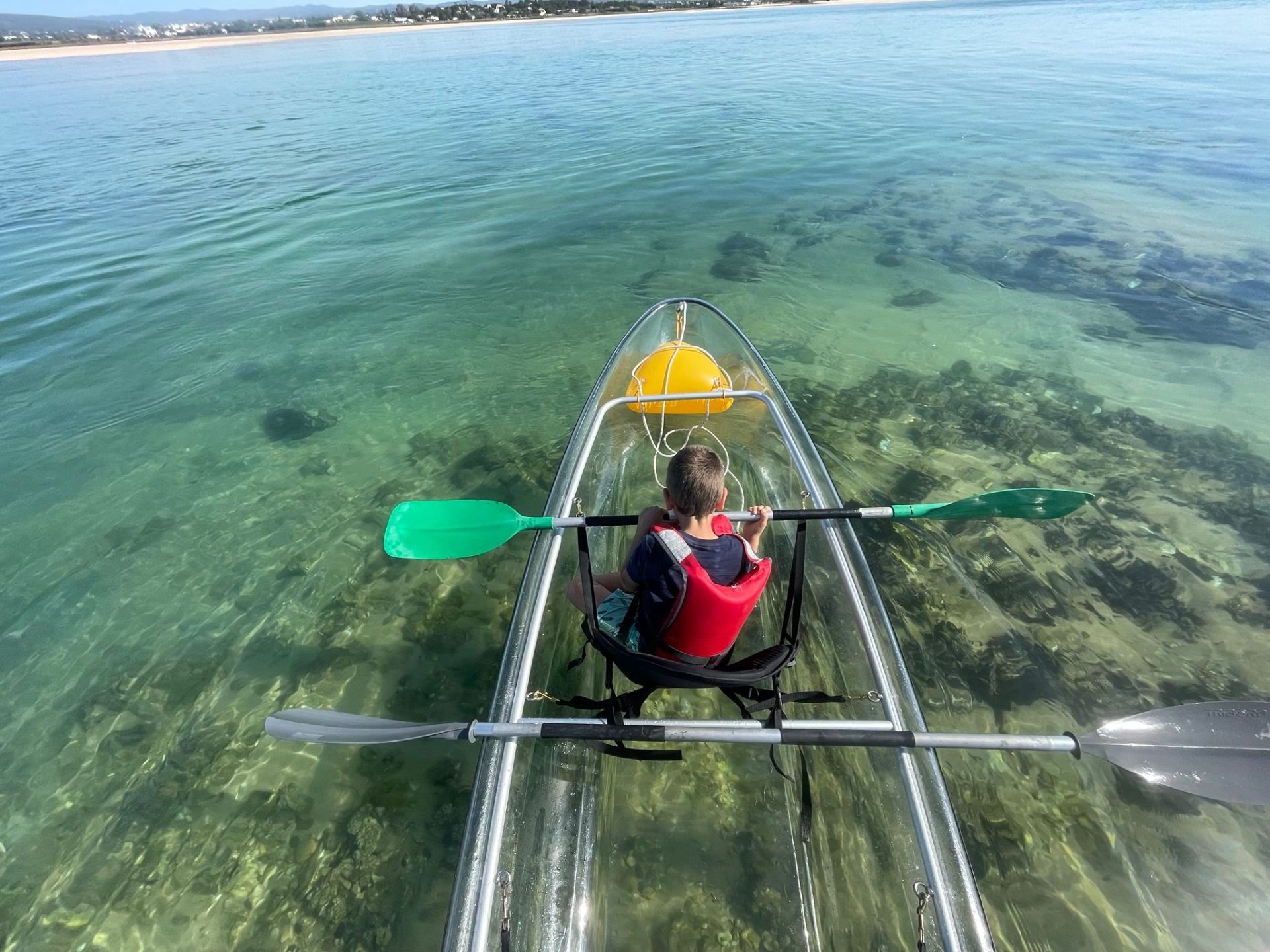 A child in a transparent kayak; seagrass and stones are visible through the hull.