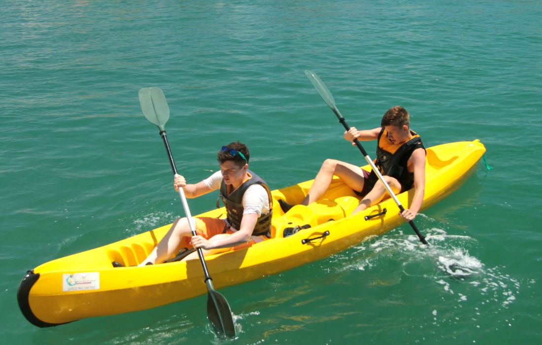 Two people paddling a yellow double kayak on green lagoon water.
